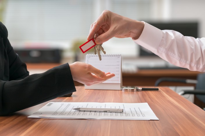 Real estate concept. Realtor is passing keys to the client sitting behind desk on blurred background.
